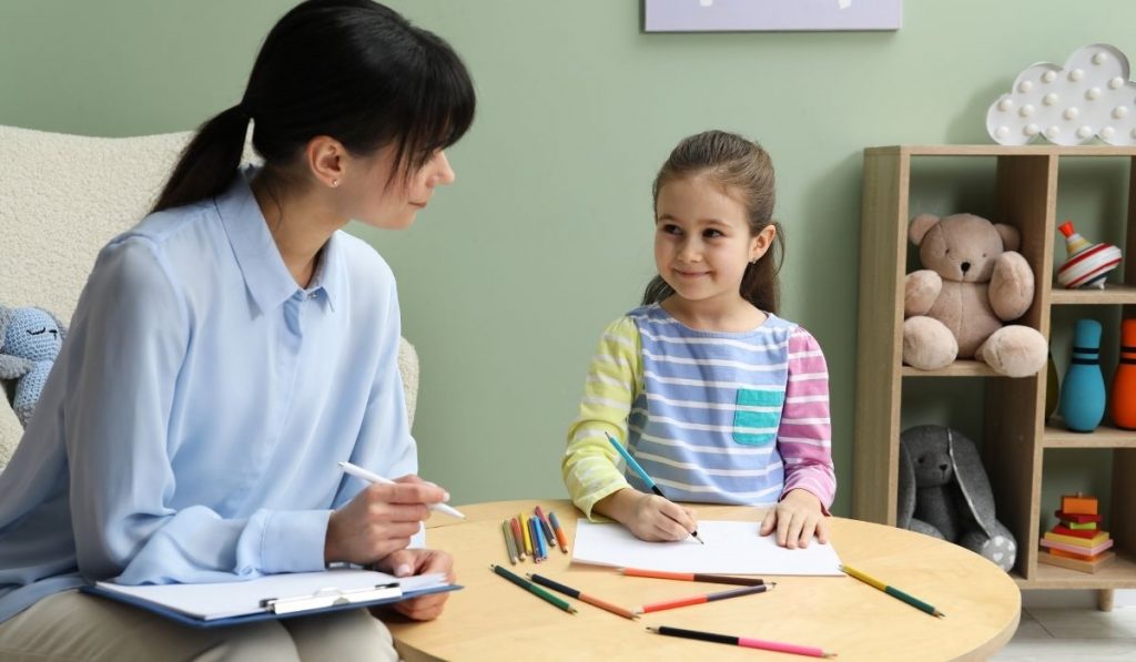 Child and therapist smile at each other at table