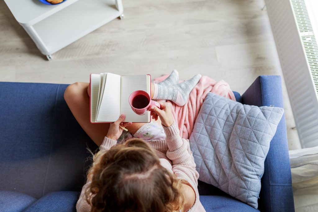 Girl on sofa reading a book with a cup of tea