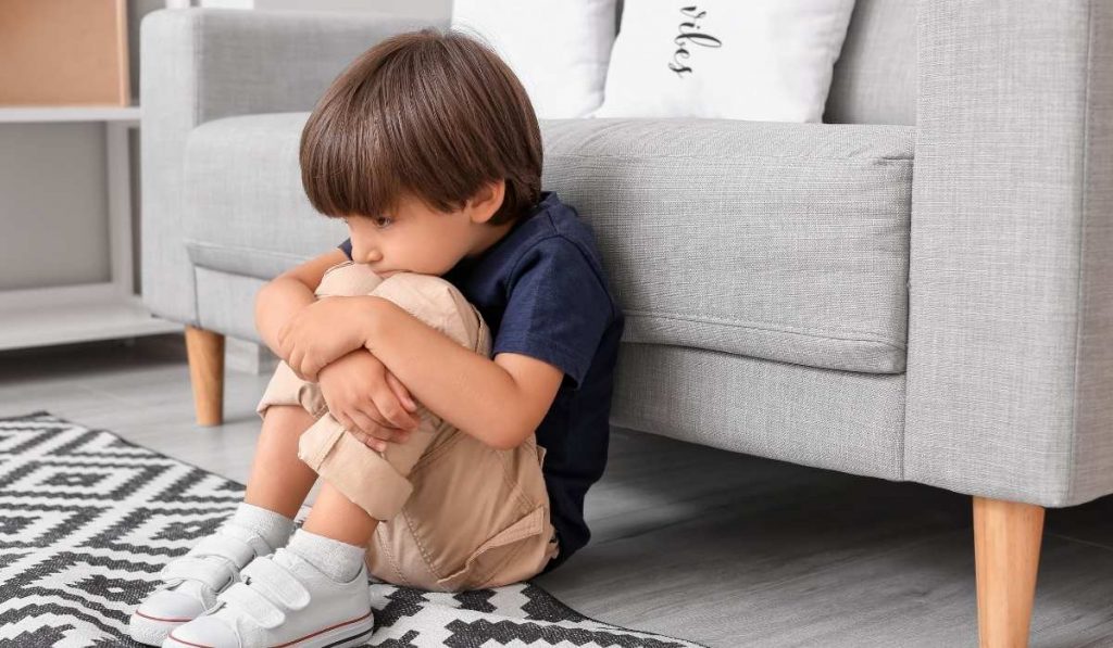 Child huddles on the floor in front of the couch