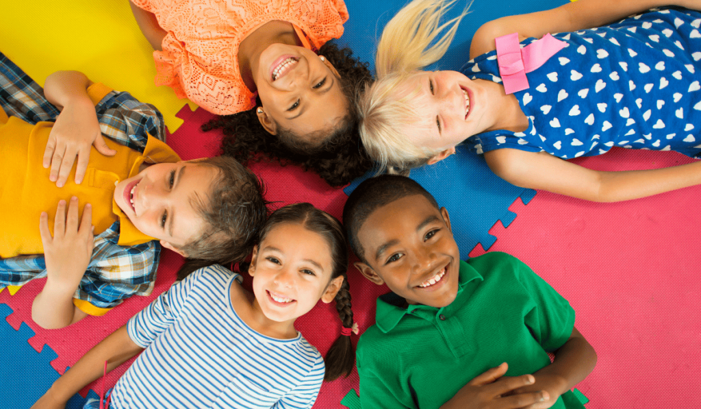 group of kids lying on colorful mat smiling at camera