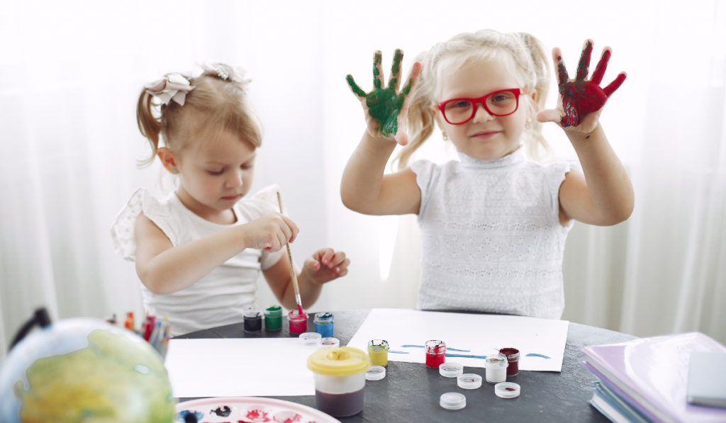 Girls painting, one with paint-covered hands